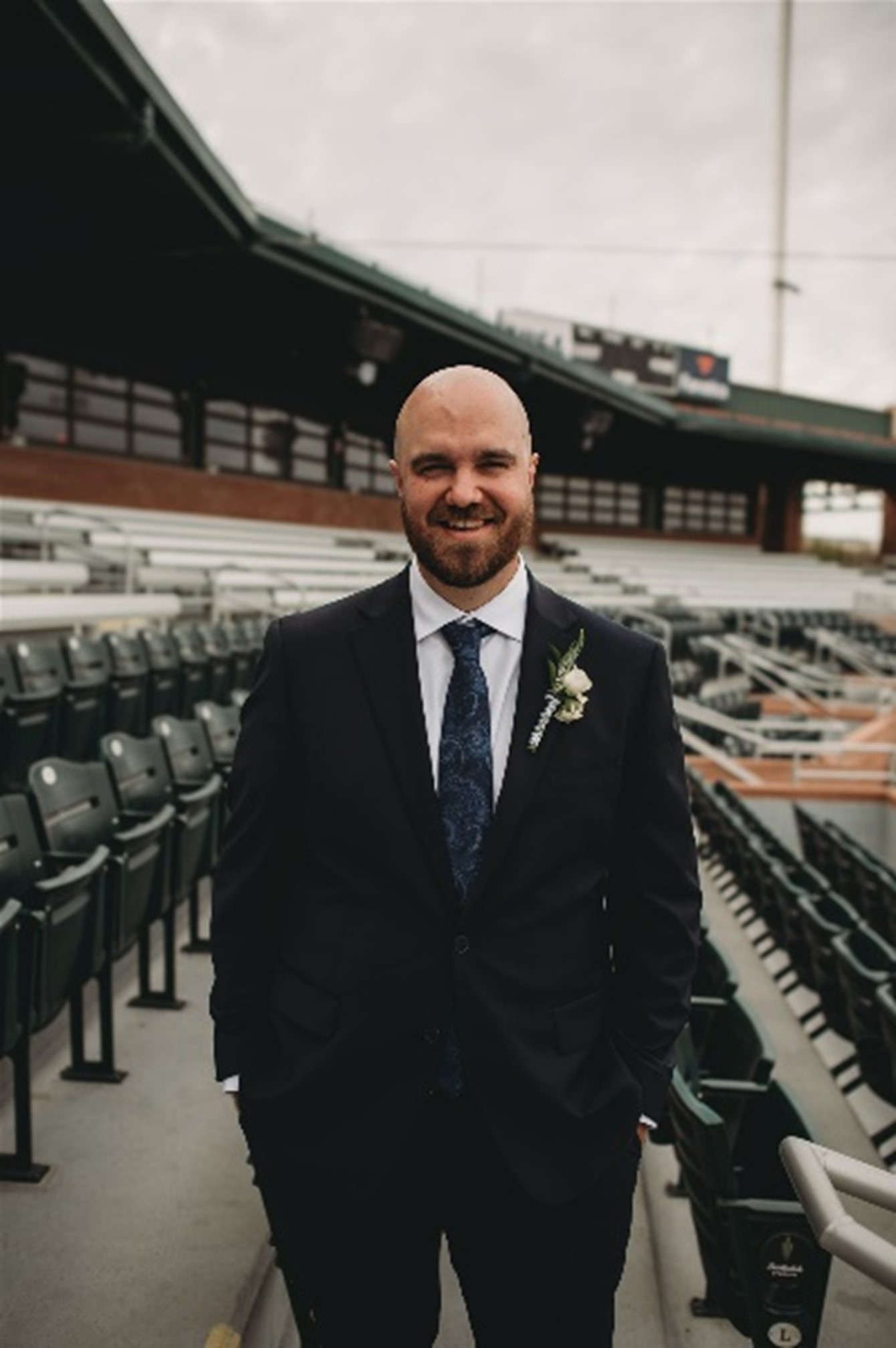 Kyle posing in business attire on the stands of an outdoor sports stadium.