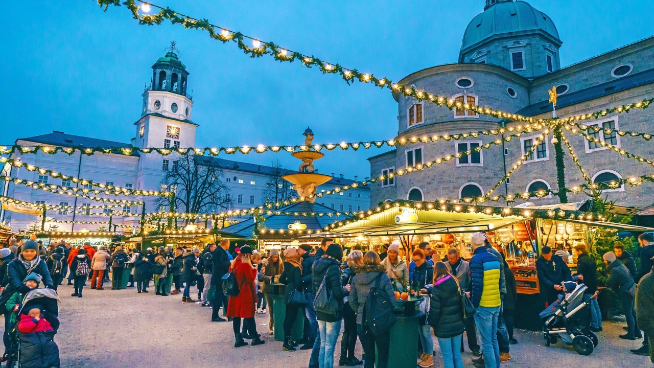Festive market scene at dusk, crowded with people under twinkling lights.