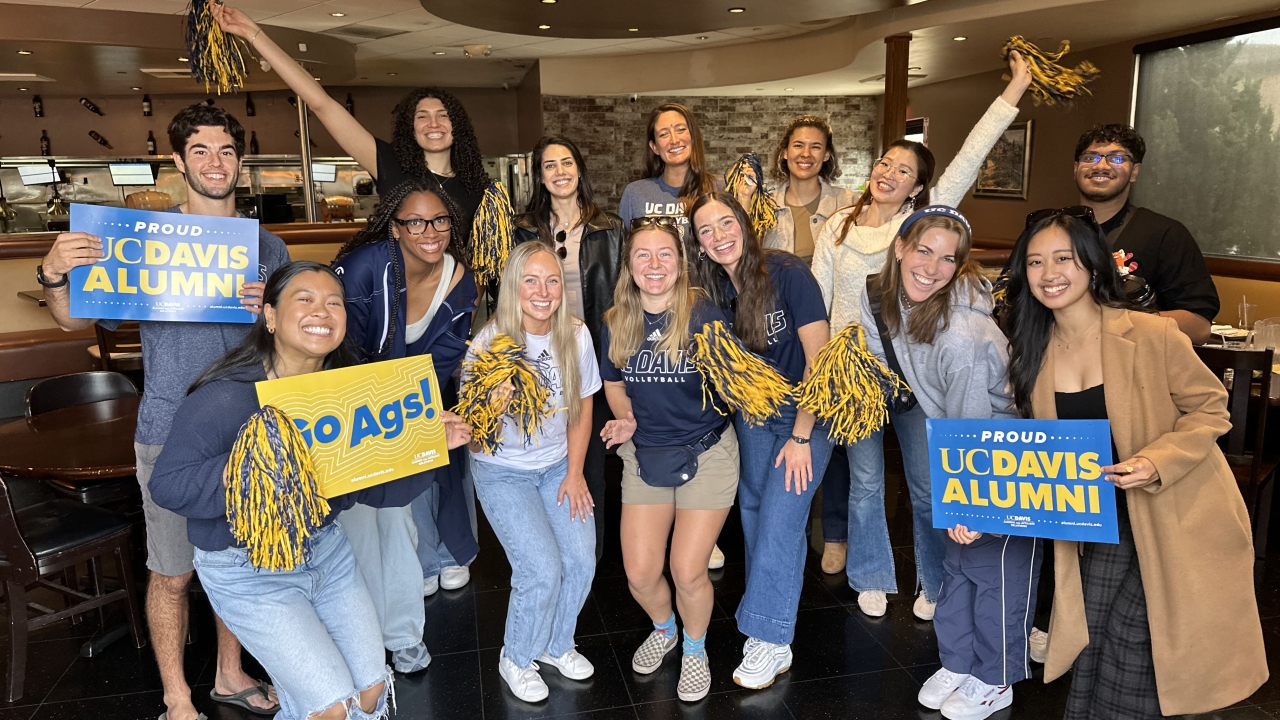 Group of people facing the camera holding blue & gold pompoms and cheer cards