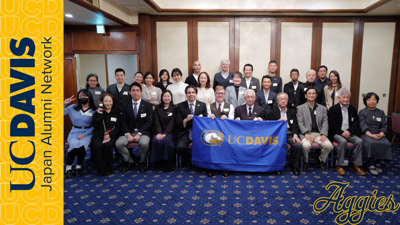 Group of about 35 UC Davis alumni and students indoors, blue UC Davis logo banner.