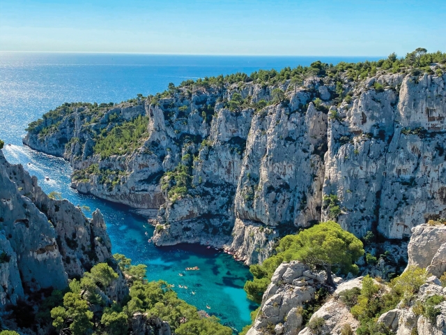 Cascading cliffs surround a turquoise cove under a bright blue sky.