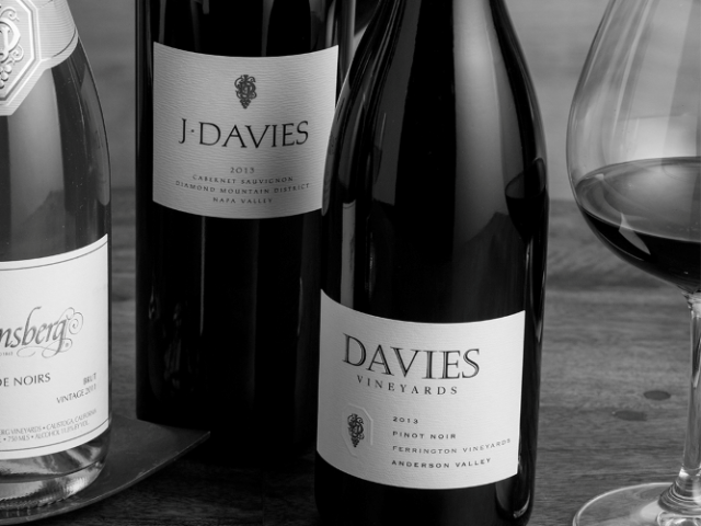 Black-and-white photo of Davies wine bottles and a filled wine glass on a wooden table