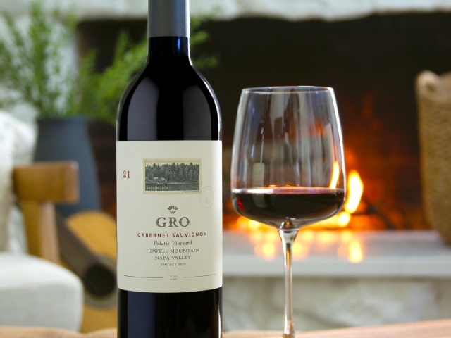 Bottle and glass of red wine on a table with a glowing fireplace in the background