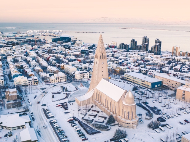 Aerial view of a snowy cityscape with a prominent church and ocean in the background.