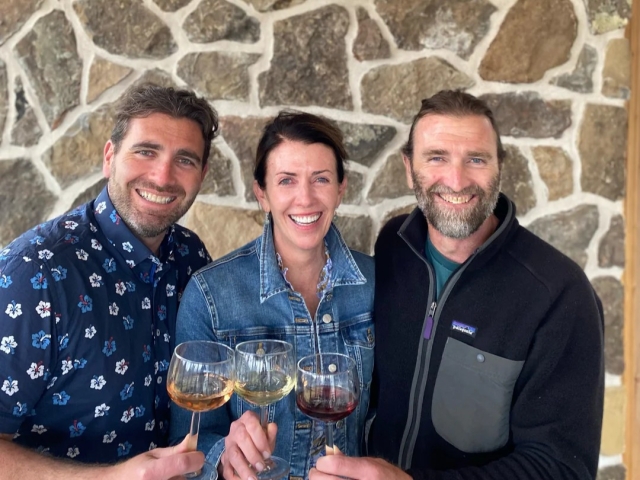 Three smiling friends toasting with wine glasses against a stone wall
