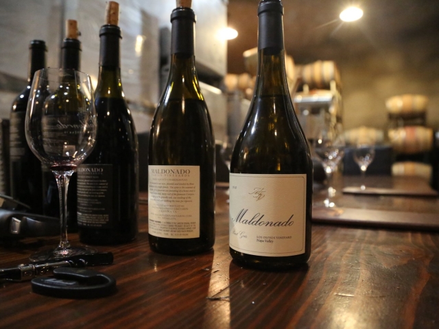 Two wine bottles and stemmed glasses on a wooden bar under warm, dim lighting