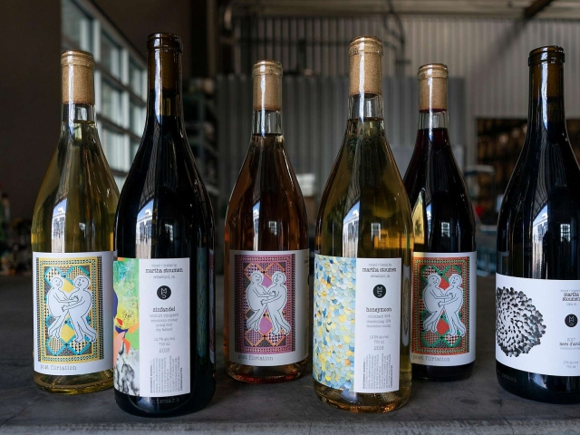 Six assorted wine bottles with colorful artistic labels on a winery counter