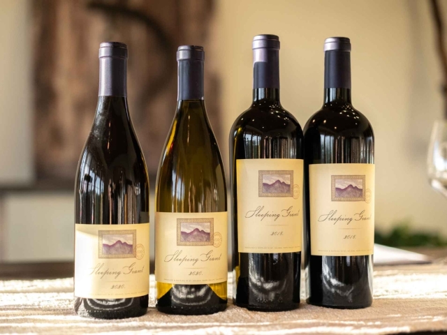 Four wine bottles with cream labels on a wooden table, warm blurred background
