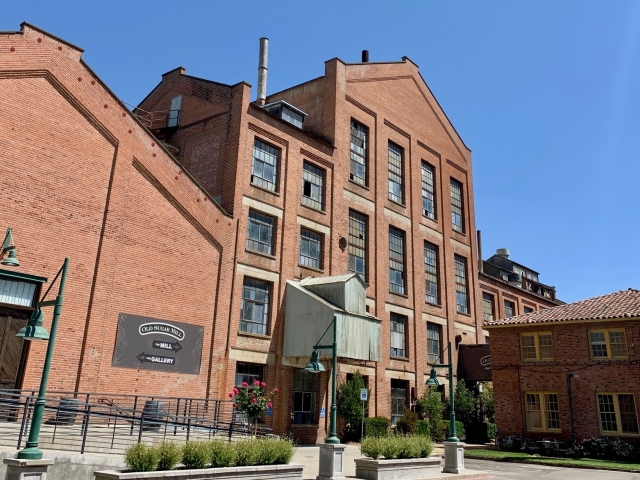 Red-brick multi-story building with glass entrance and small landscaped courtyard under blue sky