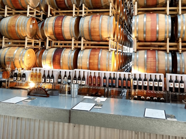 Winery tasting bar with stacked oak barrels, a row of wine bottles and menus on the counter