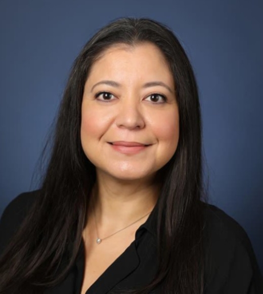 Professional headshot of a smiling woman with long dark hair, black blouse, blue backdrop