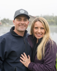 Jeff and Karen pose outdoors in softshell jackets with a body of water visible behind them.