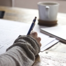 Hand holding a pen writing on paper on a desk with coffee nearby