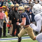 UC Davis football players runs with the ball with a Sac State player in the foreground chasing him