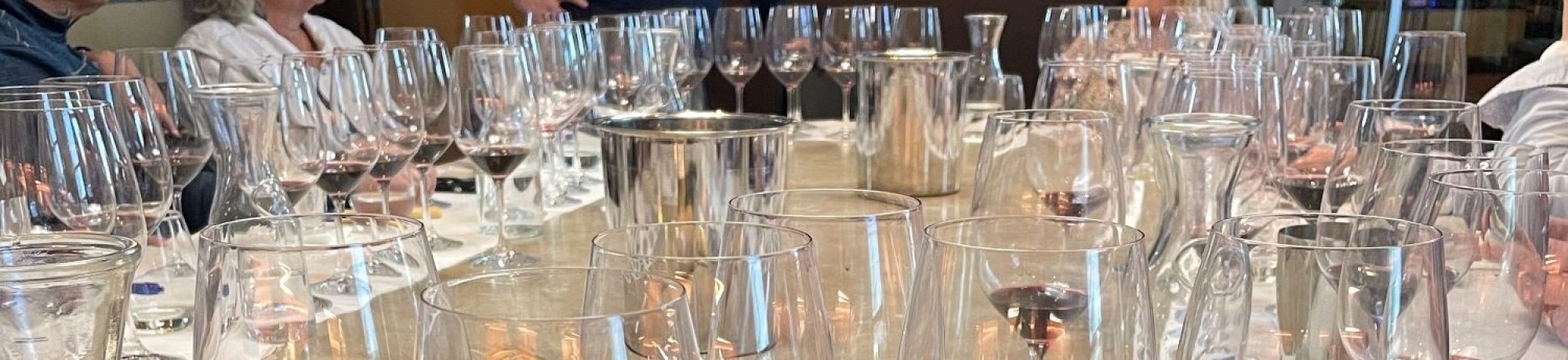 A dining table set with numerous wine glasses and a few people in the background.